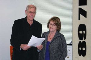 A man and a woman read from a piece of paper. To the left of them is the 89 7FM logo on the wall.