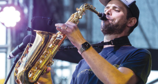 A man wearing a cap playing saxophone on stage.