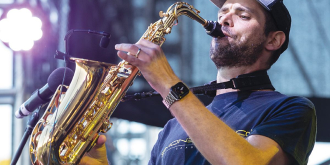 A man wearing a cap playing saxophone on stage.
